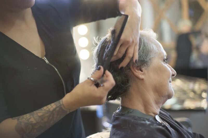 A hairstylist carefully cutting the hair of an older woman in a calm salon setting, showing a one-on-one personalized service.