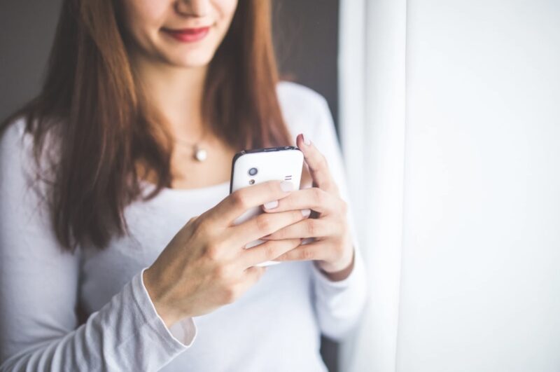 Close-up of a woman smiling while using her smartphone near a window