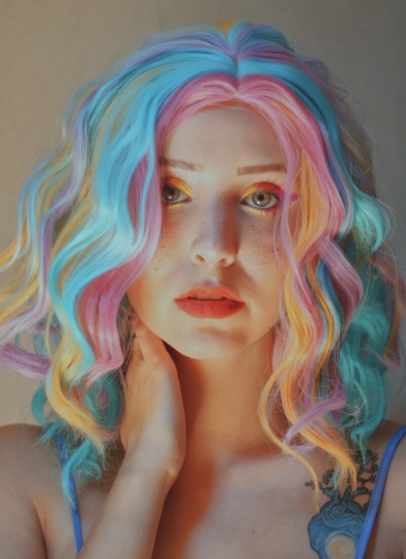 A colorful wavy hairstyle featuring vibrant bleach shades of pink, blue, and yellow. The look is bold, artistic, and highly expressive.