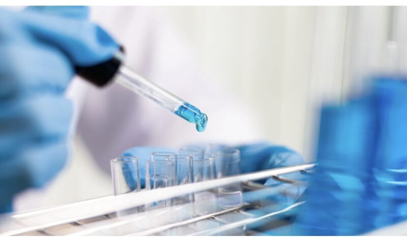 A laboratory scene with blue liquid being dropped into test tubes using a pipette