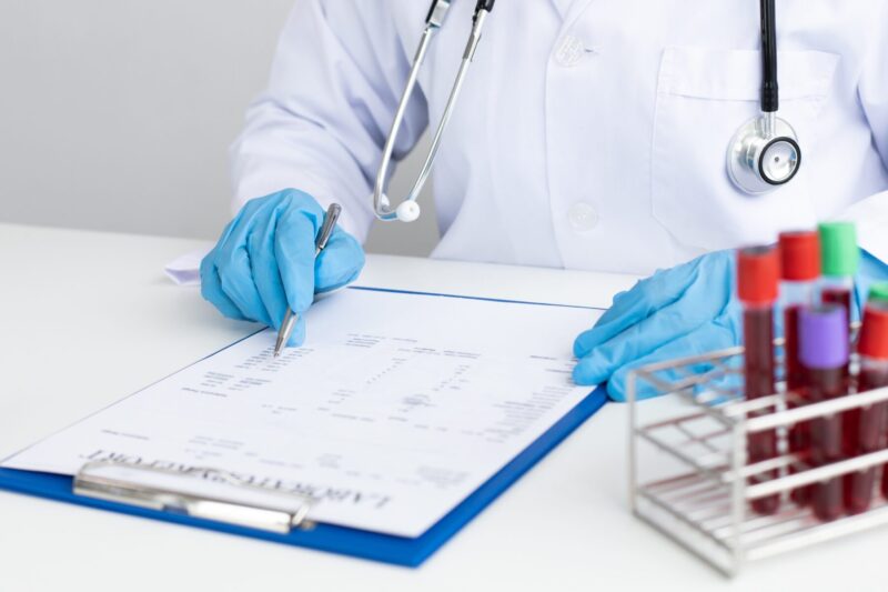 A doctor wearing blue gloves is writing on a medical report beside several blood samples, creating a calm yet professional medical atmosphere.