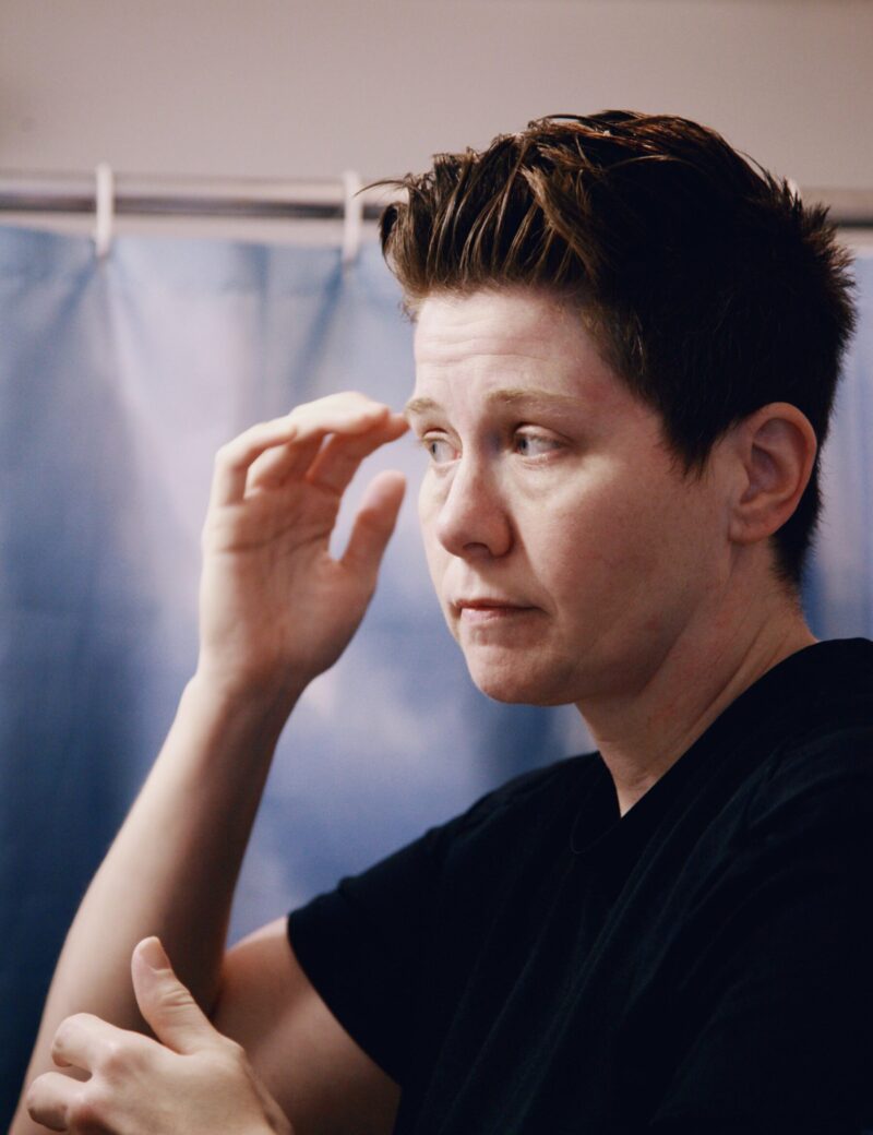 A person with short styled hair adjusting their bangs while looking in the mirror
