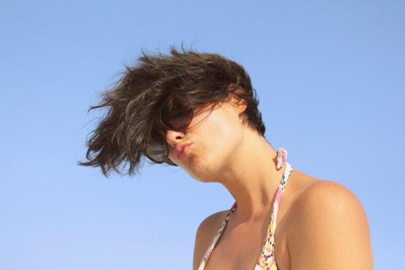 Short hairstyle with natural volume created by the wind. A woman wearing sunglasses outdoors, showing movement and texture in her hair
