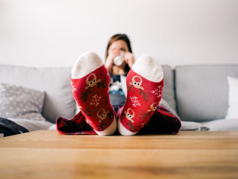  A person relaxing on a sofa with their feet on a table, wearing red patterned socks and drinking a beverage